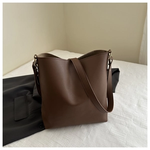 Close-up of brown leather bucket bag on white linen with stylish black blazer accent