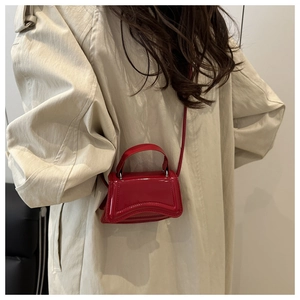 Détail du mini sac bandoulière rouge brillant porté avec un trench-coat beige élégant