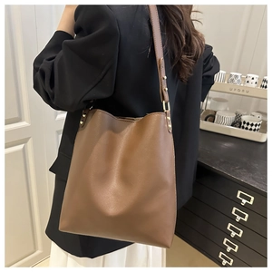 Detail of dark brown leather bucket bag with gold hardware worn by a model in a suit