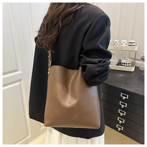 Close-up of a large brown leather bucket bag worn by a model in a minimalist home setting