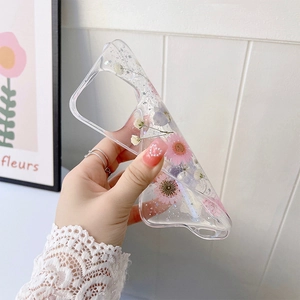 Détail d'une coque iPhone avec de vraies fleurs séchées roses et paillettes sur TPU clair