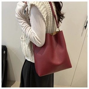 Detail of dark red tote bag in matte leather texture shown on shoulder with knitwear