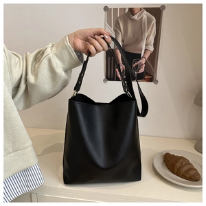 Minimalist black matte leather bucket bag held by hand to show natural drape and size