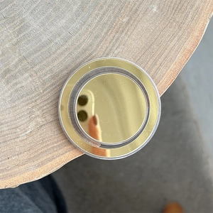Detail of round gold mirror magnetic phone grip on a natural wood surface texture