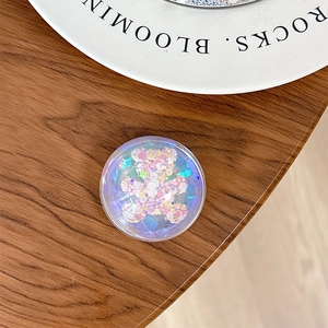 Close-up of a floral bear sequin pop socket on a white ceramic tray and wood desk