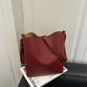 Minimalist dark red bucket shoulder bag in matte leather on a white wall and chair background