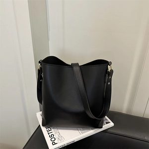 Minimalist black faux leather bucket bag with wide strap on a modern studio background