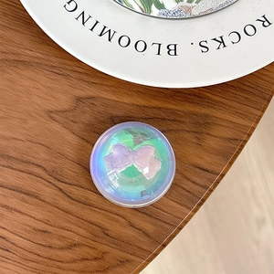 Macro view of a round iridescent phone grip holder featuring a pink 3D bow decoration