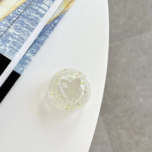 Detail of a round resin phone grip featuring yellow sequins and a silver heart mirror