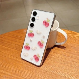 Detail of glitter white phone case with 3D red cherries, pearls and bow on a wooden table