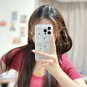 Détail de la coque iPhone transparente avec nœud strass argenté et cœurs noirs en mode selfie