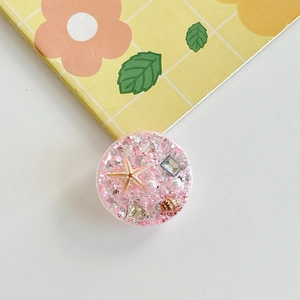 Detail of pink glitter phone grip with starfish, sea shells and pearls on resin surface