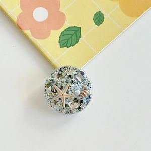 Detail of round phone grip with ocean starfish, shells and glitter in clear resin