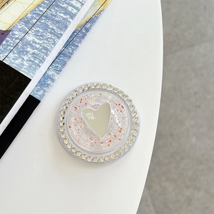 Close-up of glitter heart phone grip with rhinestones and 'mi ne.' text on white table