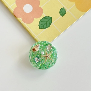 Detail of round ocean phone grip with green glitter, seashells, and pearls