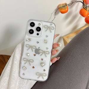 Détail d'une coque iPhone pailletée avec nœud en strass et décor de cœur miroir