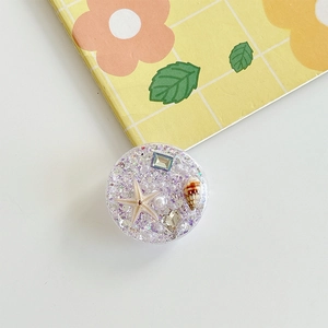 Detail of round ocean-style phone grip with purple glitter, seashells, and pearls