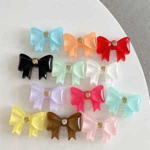 Flat lay of 12 colorful resin bow-shaped phone grips with gold heart center on white background
