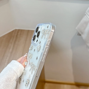 Détail de coque iPhone transparente avec nœuds en strass 3D et breloques en métal cœur