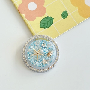Close-up of ocean-themed phone grip with blue glitter, shells, and starfish details