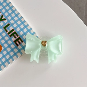 Close-up of mint green bow phone grip tok with a gold heart and transparent base