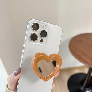 Handheld heart-shaped phone grip with integrated mirror on a white smartphone