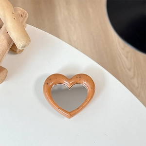 Detail of heart-shaped phone grip mirror with orange tortoiseshell pattern on wood