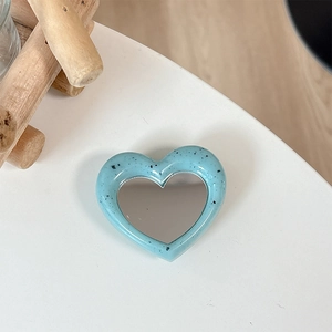 Macro detail of heart-shaped light blue mirror phone stand with chic black ink splatter effect
