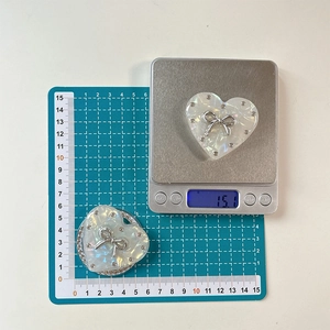 Detail showing pearlescent heart phone stand weight and size with silver bow