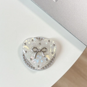 Detail of heart-shaped magnetic phone grip with rhinestone bow and mother of pearl finish
