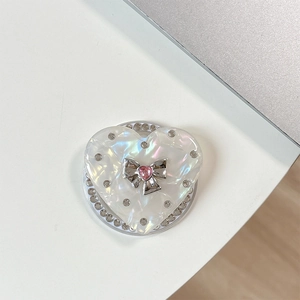 Detail view of heart-shaped phone grip with pearl texture, silver bow, and pink crystal