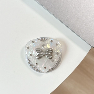 Detail of heart-shaped phone grip featuring pearl texture, silver bow, and rhinestones