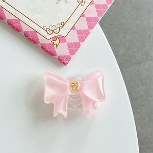 Macro detail of pink resin bow phone grip with elegant golden emblem on white surface