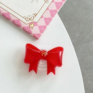 Detailed close-up of a red glossy bow phone grip with delicate gold emblem on white surface