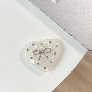 Detail of heart-shaped phone grip with iridescent texture and rhinestone bow decoration