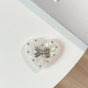 Close-up of heart-shaped phone grip with silver bow and rhinestones on pearlescent resin