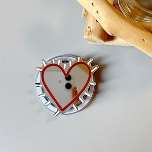 Detail of heart mirror phone grip with red trim and silver spikes on folding base