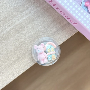 Detail shot of a clear round phone grip with 3D miniature bear and blue house models