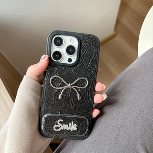 Detail of black leather texture phone case with silver metal bow and rhinestone smile charm