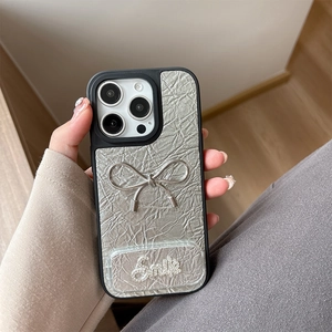 Close-up of silver wrinkled leather iPhone case with a 3D metallic bow and Smile detail