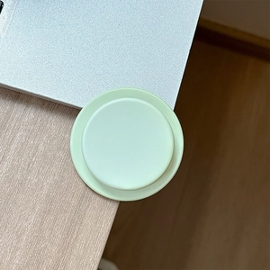Detail of a round light green magnetic airbag phone stand on a laptop corner