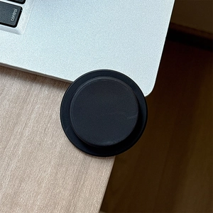 Close-up of a black circular magnetic phone grip holder on a light wood desk surface