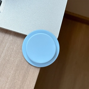 Close-up of a round light blue silicone phone socket grip on a wooden desk corner