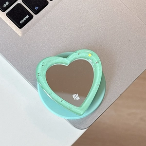 Detail of mint green glitter heart mirror phone grip with mi ne brand logo on metal surface