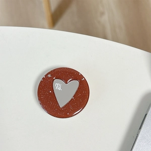 Dettaglio macro del supporto per telefono glitter marrone con specchio a cuore e scritta