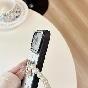 Macro shot of rhinestone camera frame and pearl chain on faux snakeskin phone case