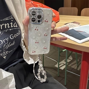 Detail of iPhone Pro case featuring red cherry charms, pearl beads, and silver camera frame