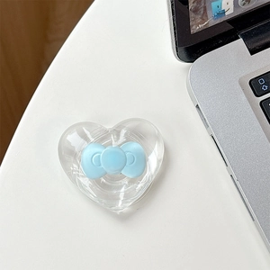 Detail showing a heart-shaped MagSafe phone grip with a light blue bow on a white desk