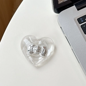 Detail of transparent heart MagSafe phone grip with silver bow accent on a desk
