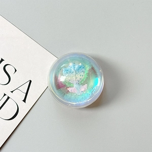 Detail of a round laser tulip phone grip with blue glitter inside on a grey surface